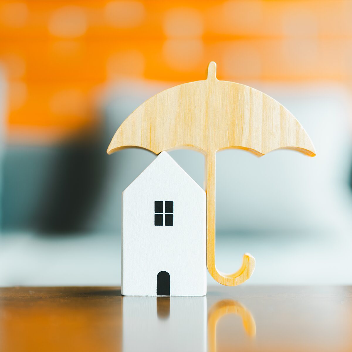 Small white house figurine under a wooden umbrella, against a blurred orange background.